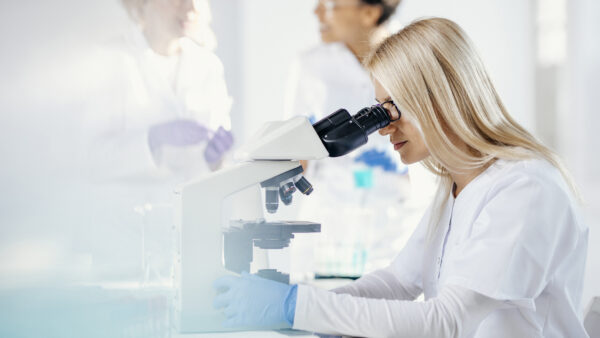 A woman in a lab coat studies samples with a microscope.